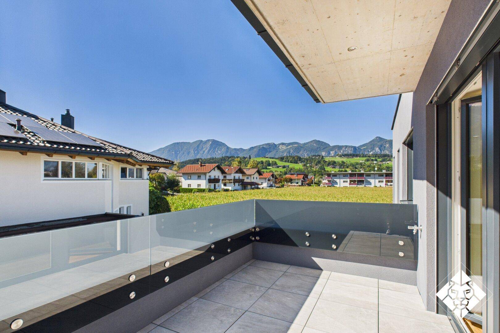 Sonniger Balkon mit Glasbrüstung und weitem Blick auf die Berge und die grüne Landschaft.