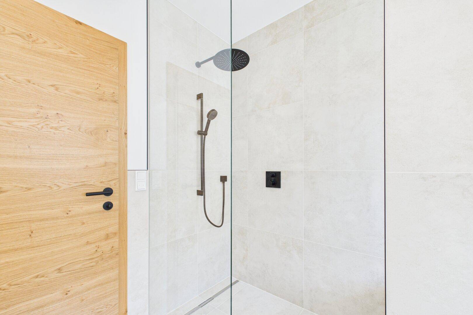 Ebenerdige Dusche mit Regenduschkopf und modernen schwarzen Armaturen in hellem Bad.