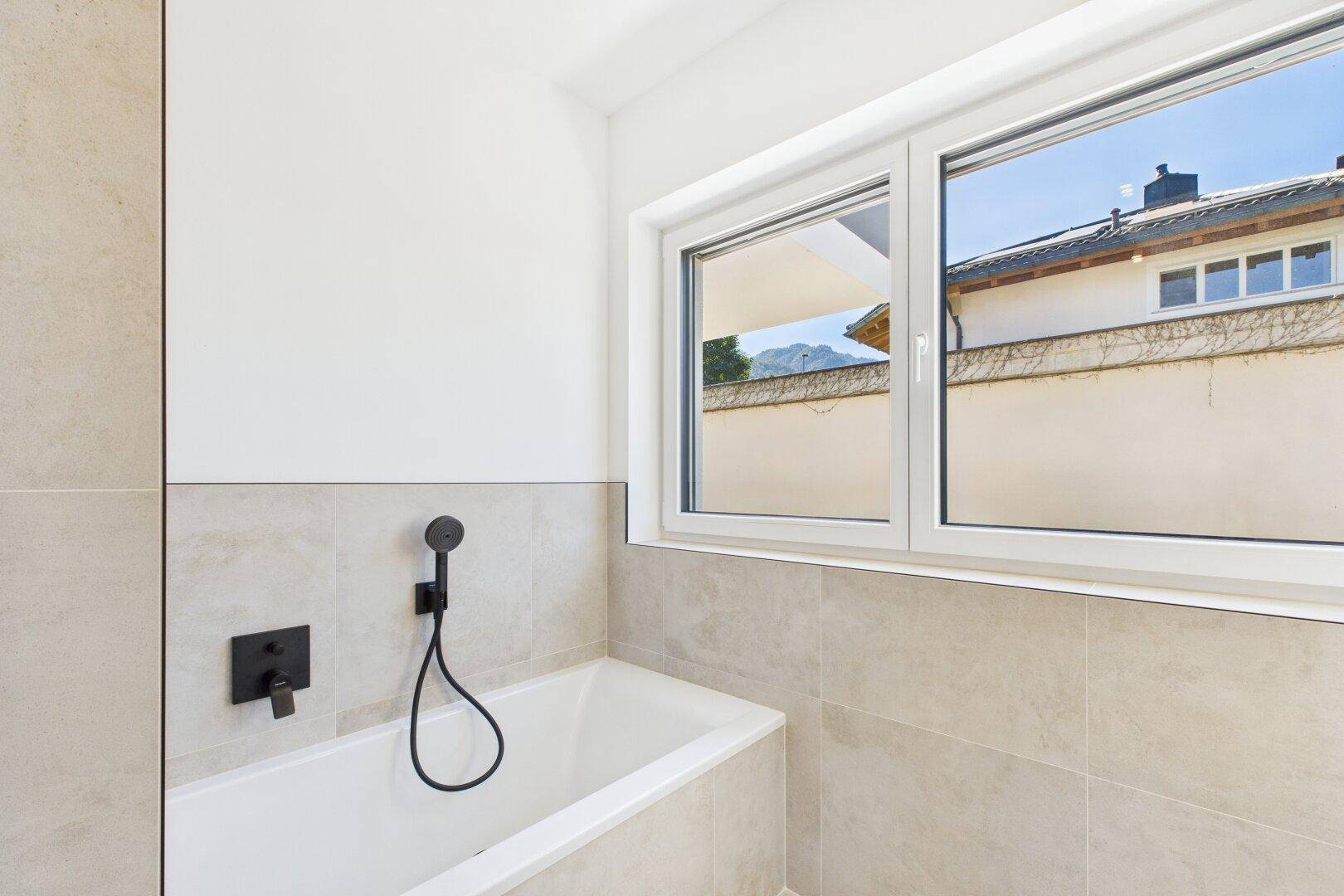 Badewanne mit Handbrause und Fenster, das Tageslicht in das moderne Badezimmer bringt.