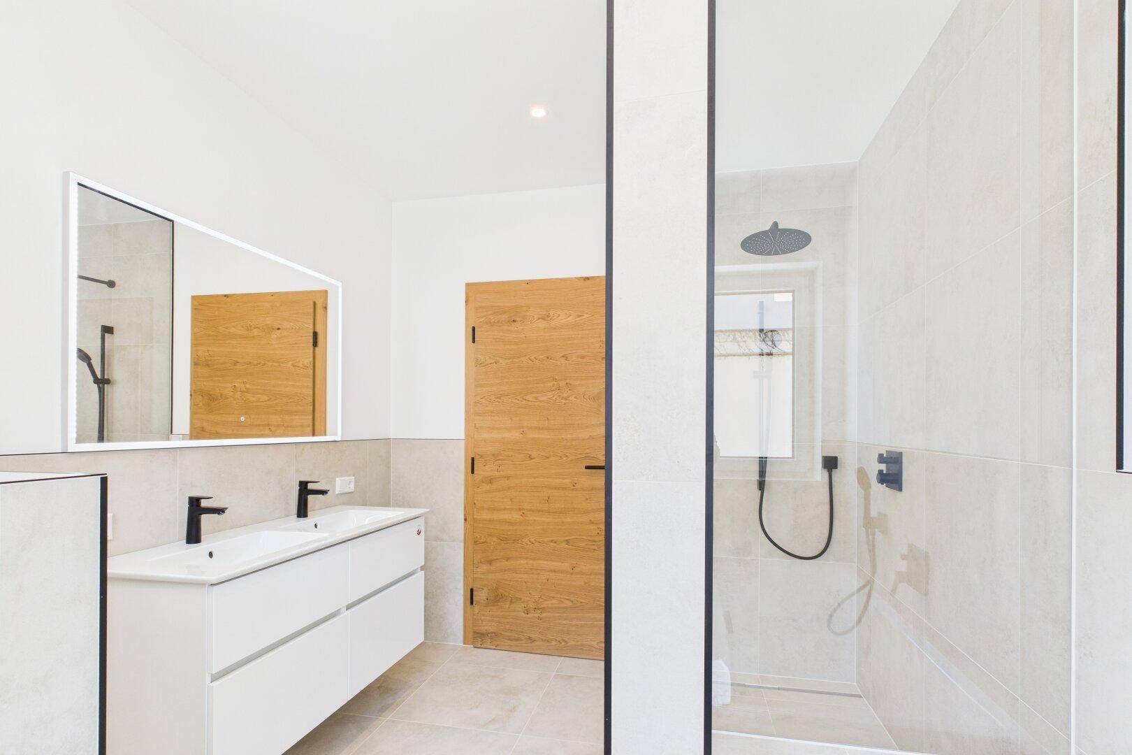 Geräumiges Badezimmer mit Doppelwaschbecken, Dusche und Holztür, modern gestaltet.