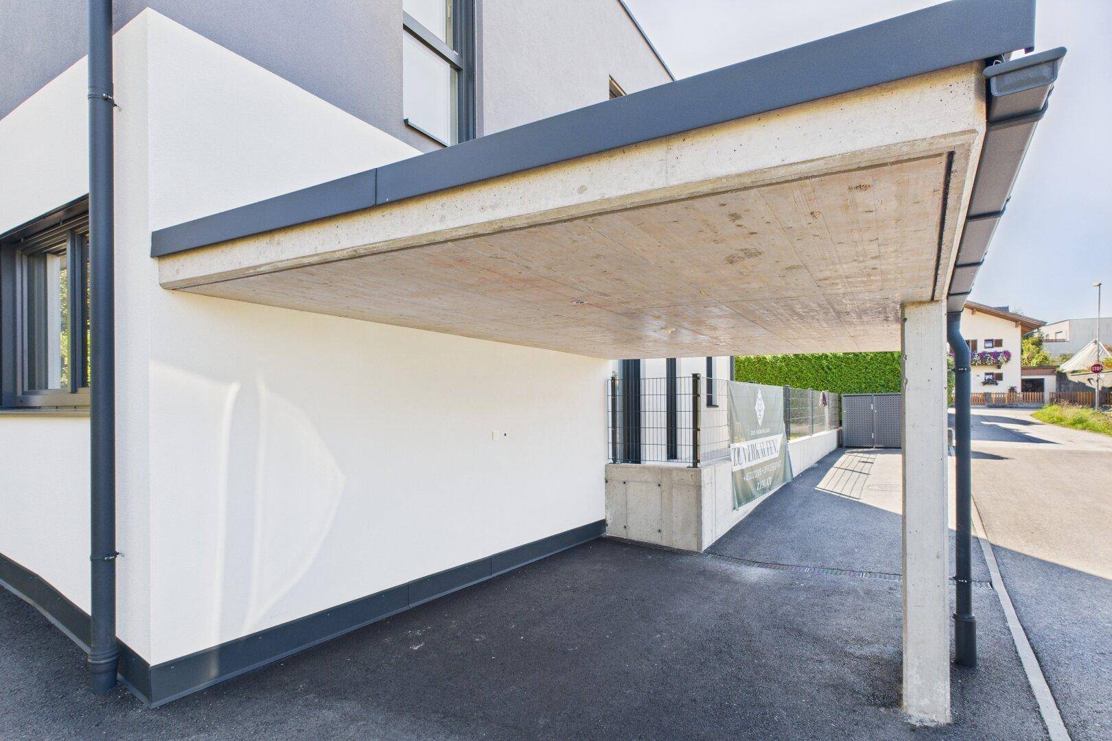 Moderner Carport aus Beton und Metall, der Schutz für ein Fahrzeug bietet.