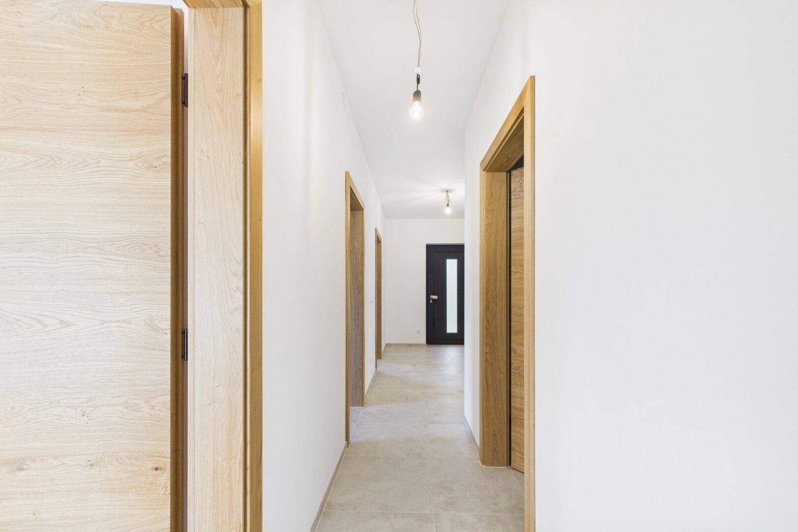 Langer, heller Flur mit Holztüren und Fliesenboden, der die verschiedenen Zimmer verbindet.
