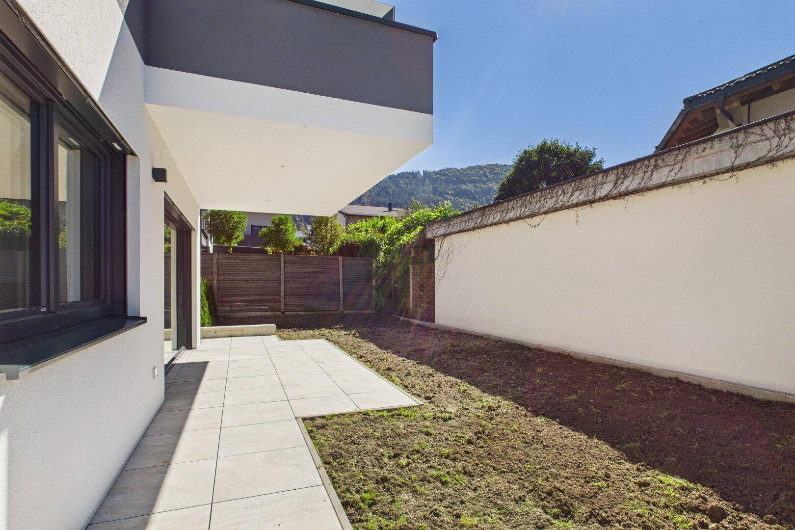 Kleine Terrasse mit angrenzendem Gartenbereich, bereit zur Bepflanzung.