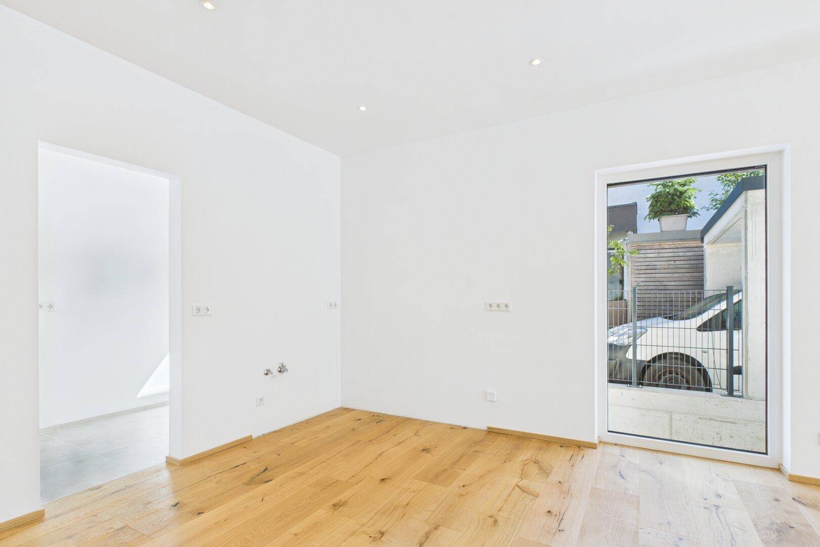 Heller Raum mit Holzboden und großer Fenstertür, die viel Tageslicht hereinlässt.