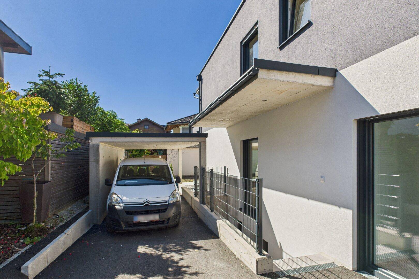 Carport mit geparktem Fahrzeug und Zugang zum modernen Wohngebäude.
