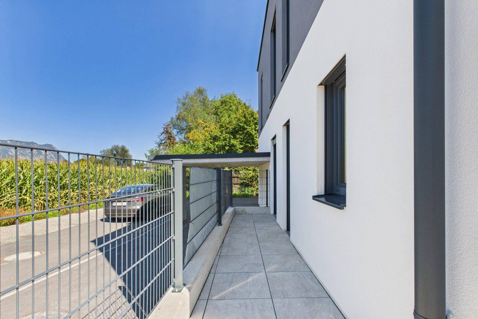 Moderne Hausfassade mit Carport und Zugang zum Grundstück, umgeben von Natur und Bergen.
