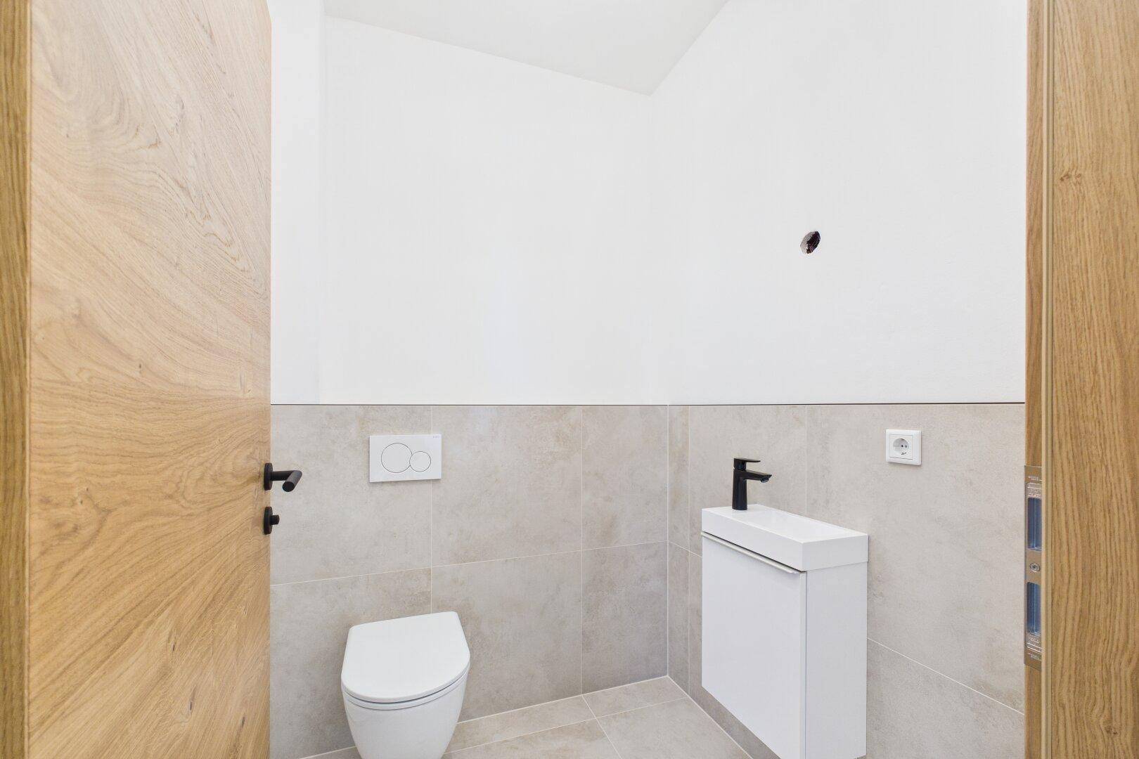 Modernes Gäste-WC mit Wand-WC, kleinem Waschbecken und hellen Fliesen.