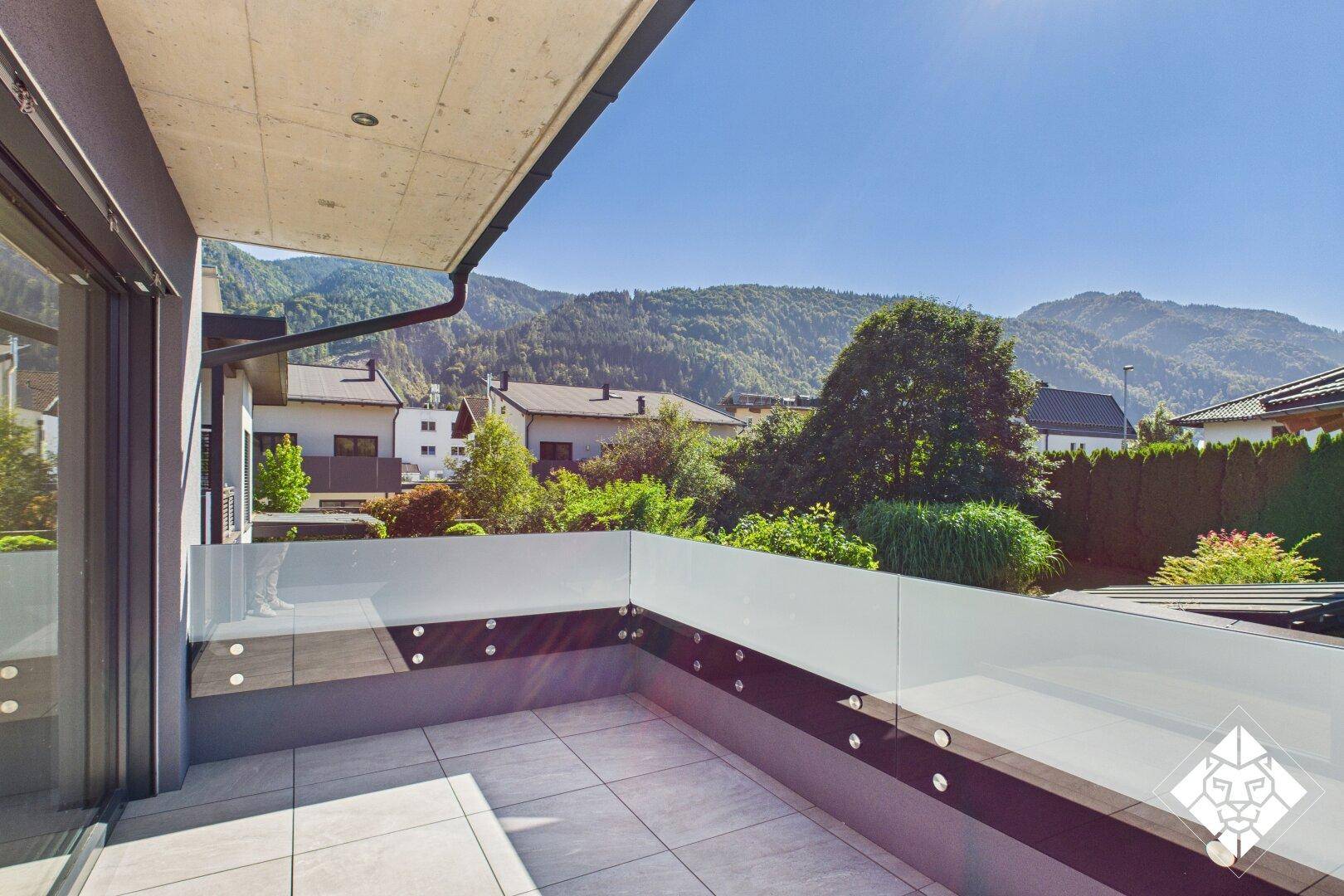 Sonniger Balkon mit Glasbrüstung und Blick auf die umliegende Berglandschaft.