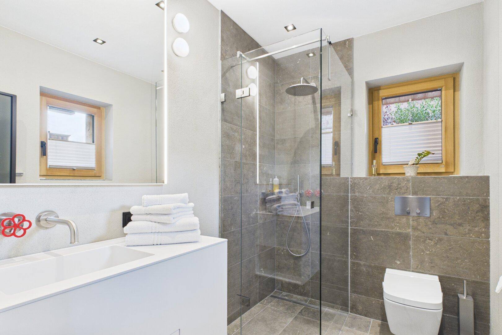 Modernes Badezimmer mit begehbarer Dusche, Wand-WC und Fenster für Tageslicht.