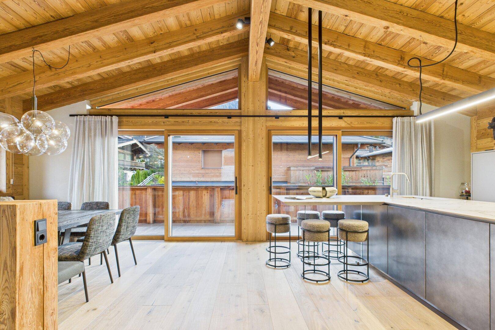 Offener Wohn-Essbereich mit moderner Küche, Holzbalkendecke und Zugang zum Balkon.