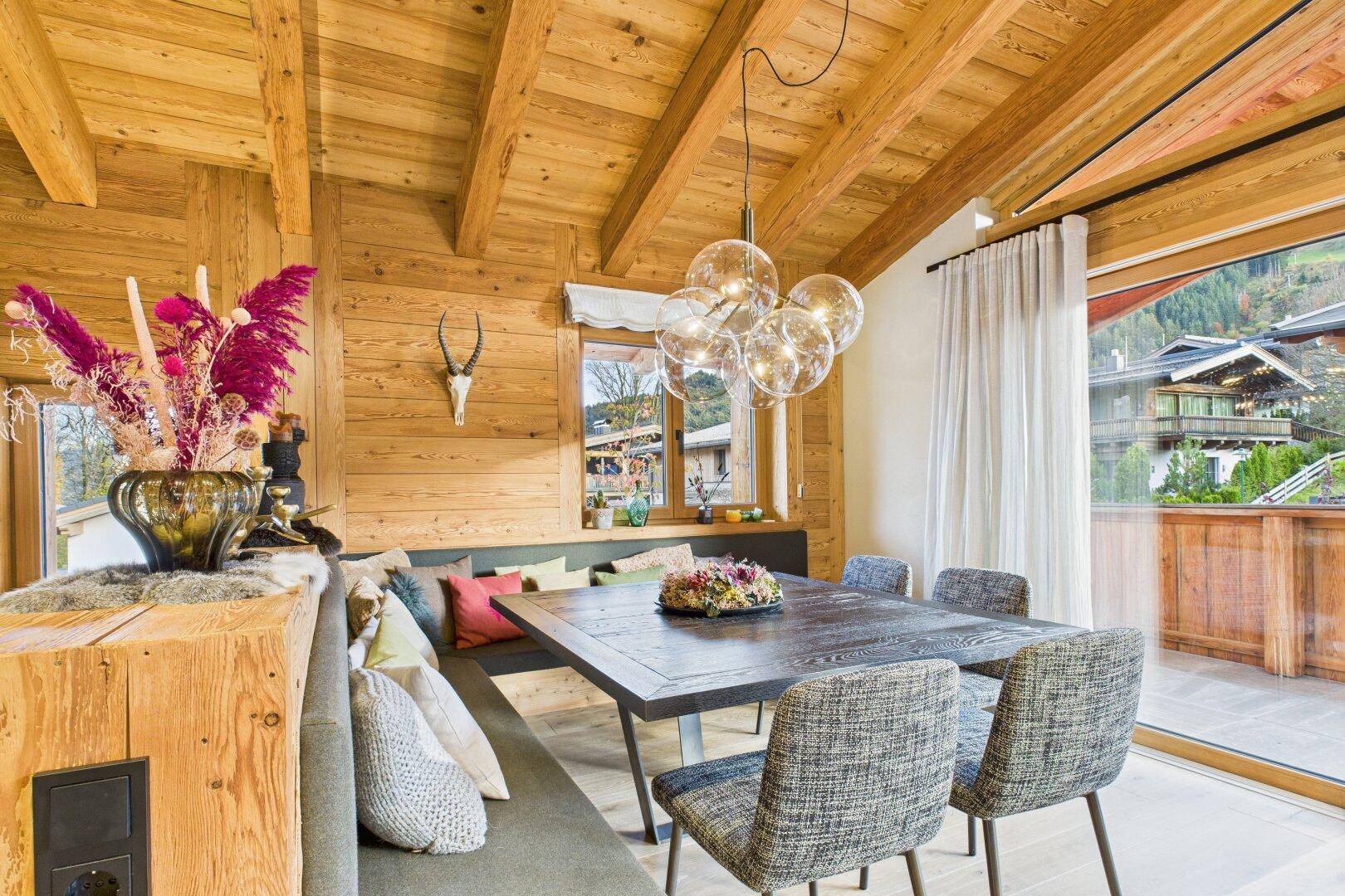 Heller Essbereich mit großem Holztisch, Holzwänden und direktem Zugang zum Balkon.