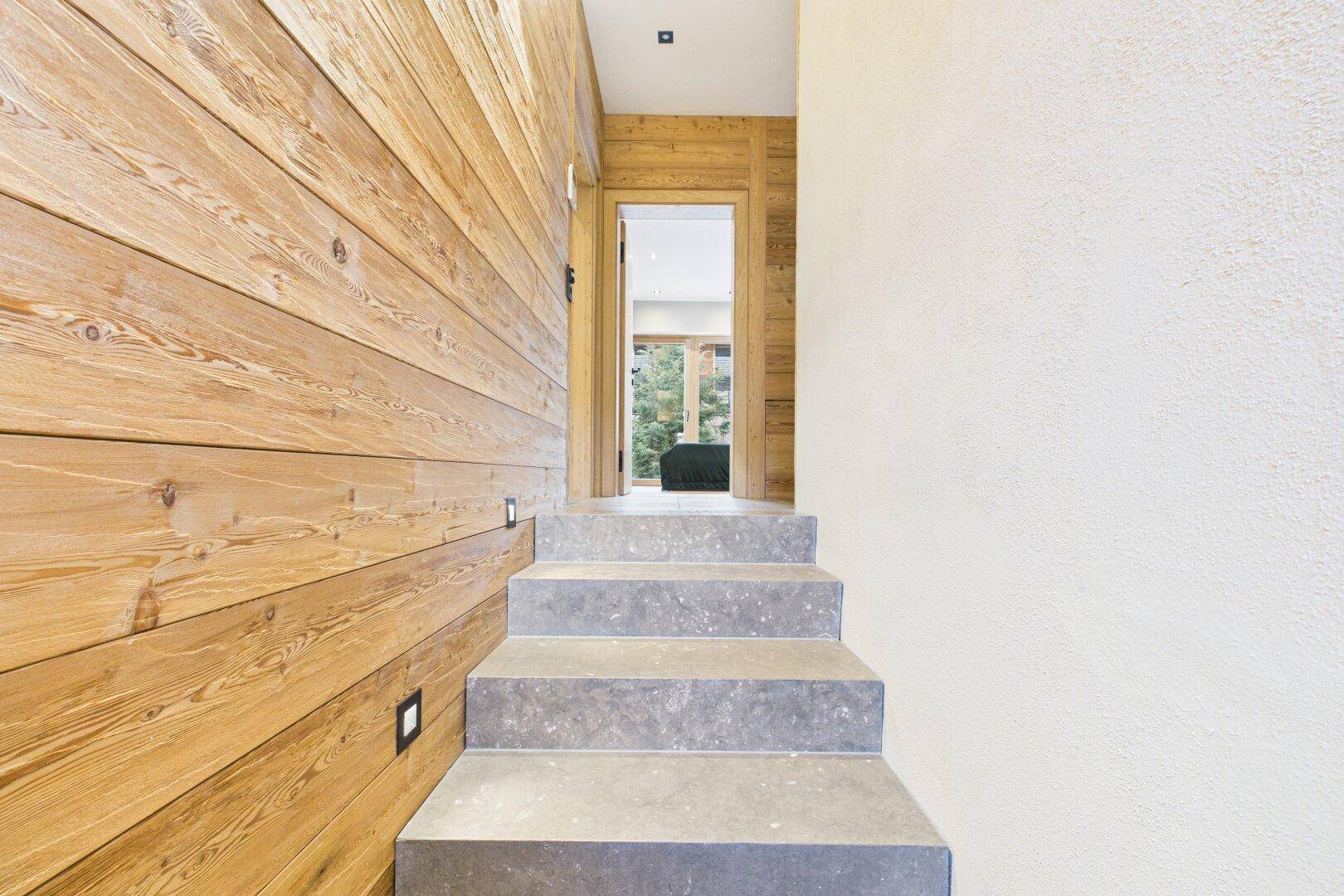 Moderner Treppenaufgang mit Steinplatten und Holzwänden, gut beleuchtet.