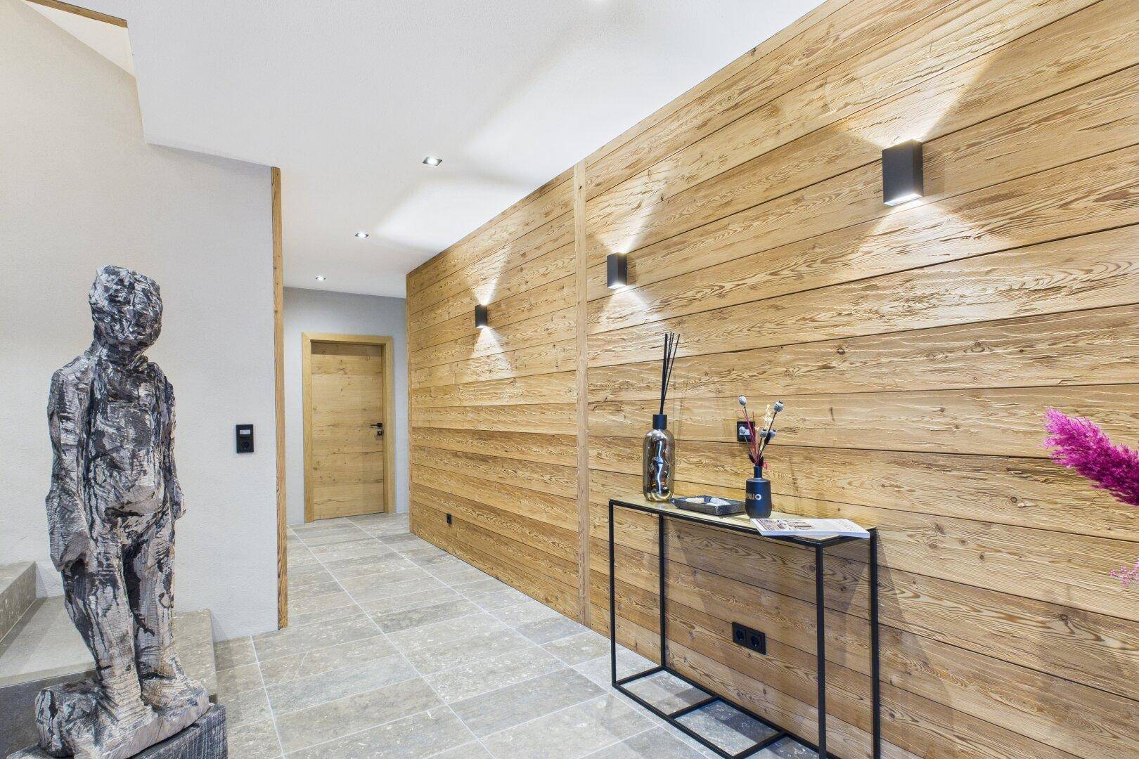Heller Flur mit Holzwänden, Steinboden und moderner Wandbeleuchtung.