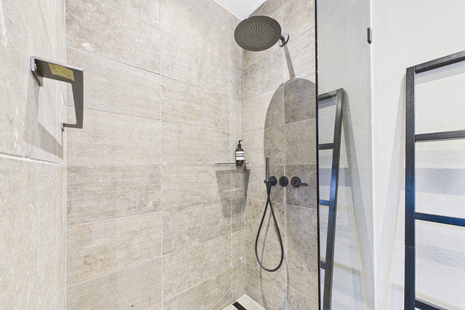 Detailansicht einer modernen, begehbaren Dusche mit Regenduschkopf und eleganten Armaturen.