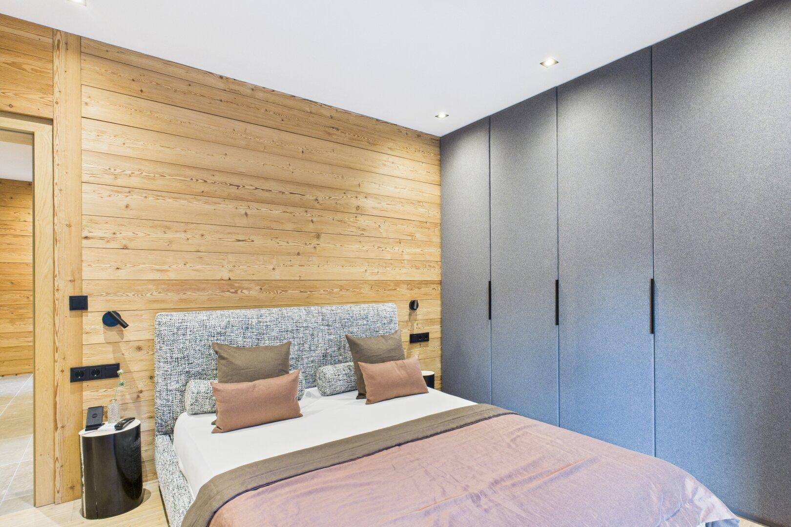 Modernes Schlafzimmer mit Holzwand, Einbauschränken und gemütlichem Doppelbett.