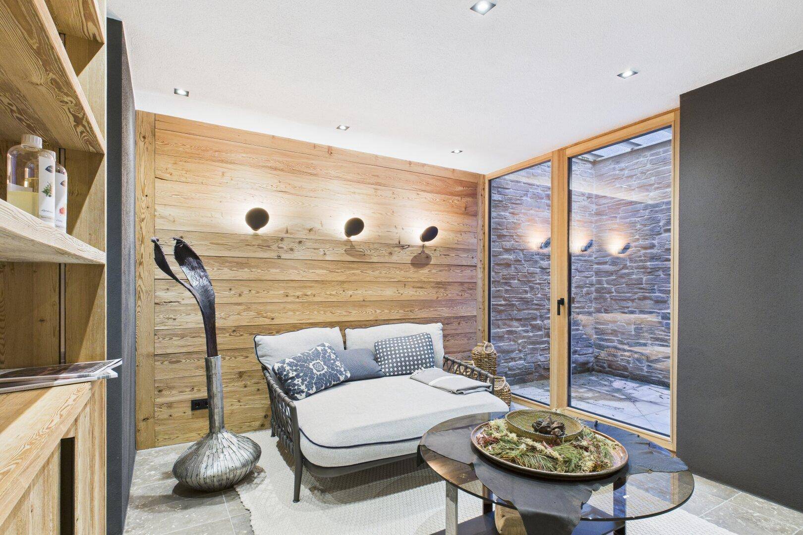 Gemütlicher Entspannungsbereich mit Holzwänden, bequemer Liege und Zugang zu einem Lichthof.