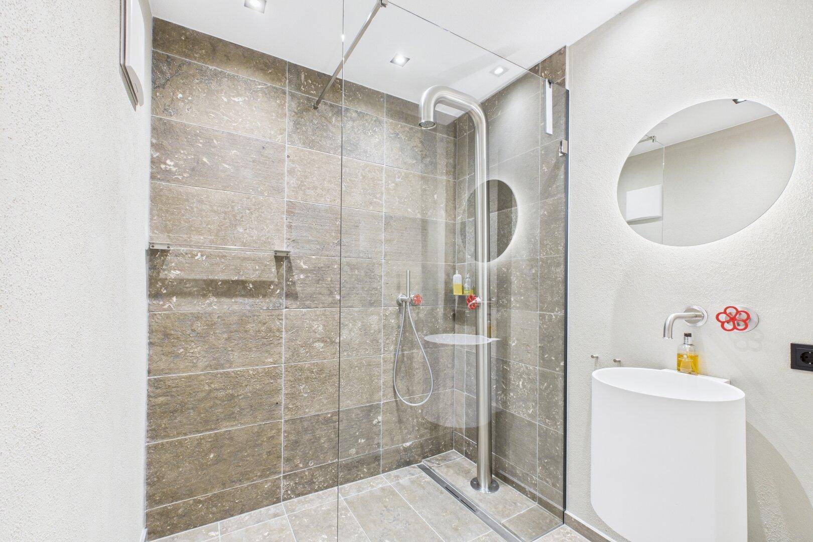 Helles Badezimmer mit begehbarer Dusche, modernem Waschtisch und runden Spiegeln.