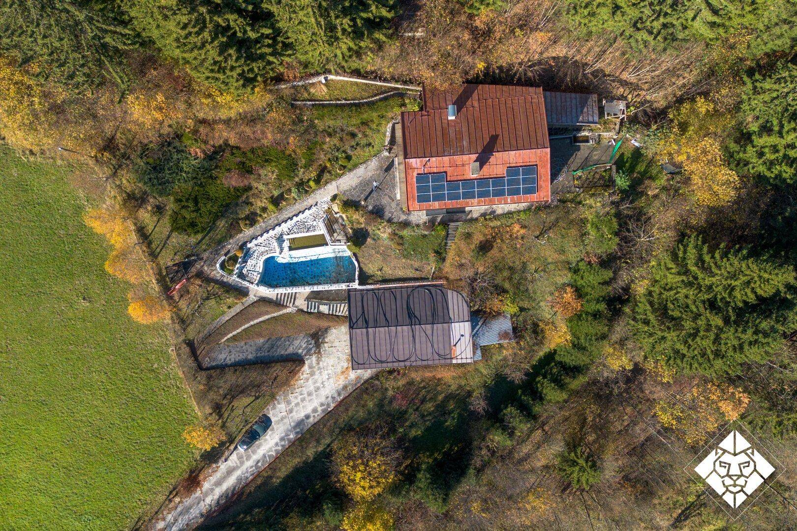 Draufsicht auf das Anwesen mit Haupthaus, Pool und Nebengebäude, umgeben von Wald und Wiesen.