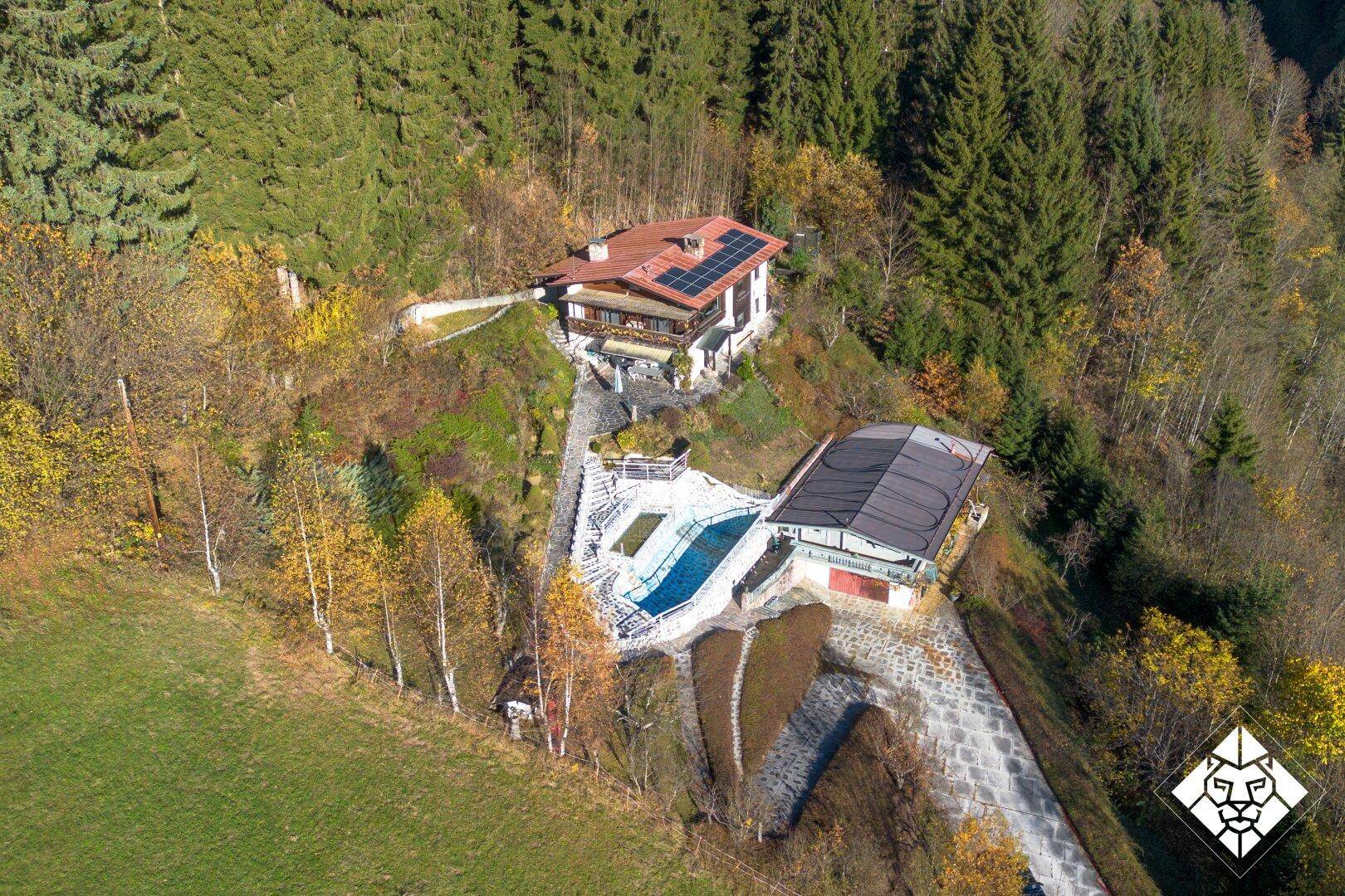 Panoramablick auf das Anwesen mit Haupthaus, Poolbereich und Nebengebäude inmitten der bewaldeten Hügel.