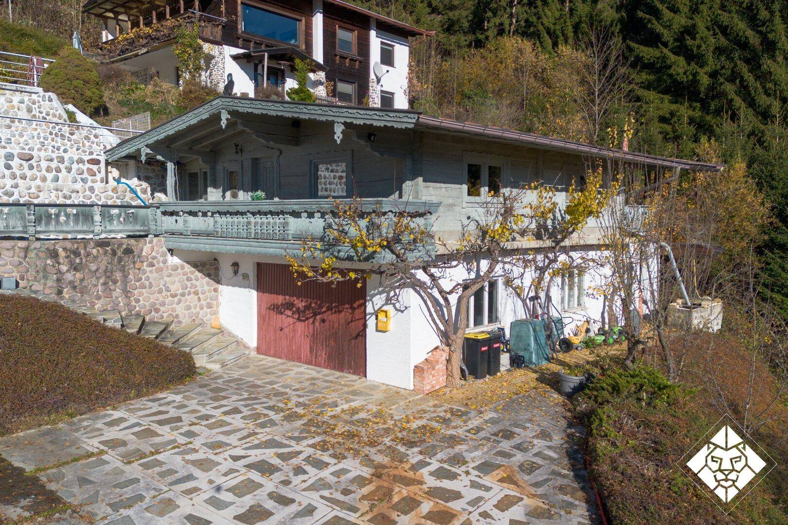 Ansicht des Nebengebäudes mit Garage und traditionellem Holzbalkon, umgeben von Steinmauern.