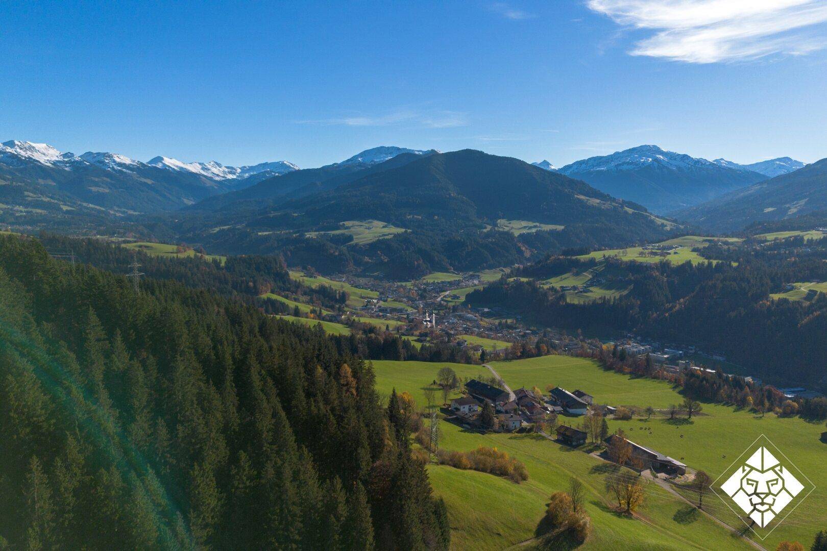 Weitläufiger Panoramablick über das Tal mit grünen Wiesen und schneebedeckten Bergen im Hintergrund.