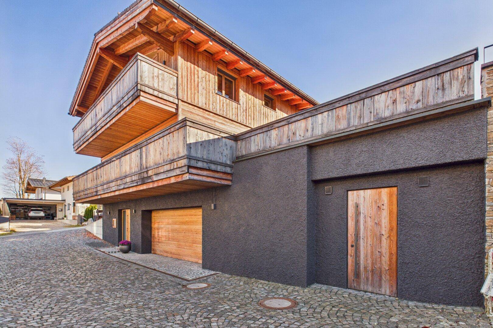 Detailansicht der Garageneinfahrt und des Eingangs des Holzchalets mit Natursteinpflaster.