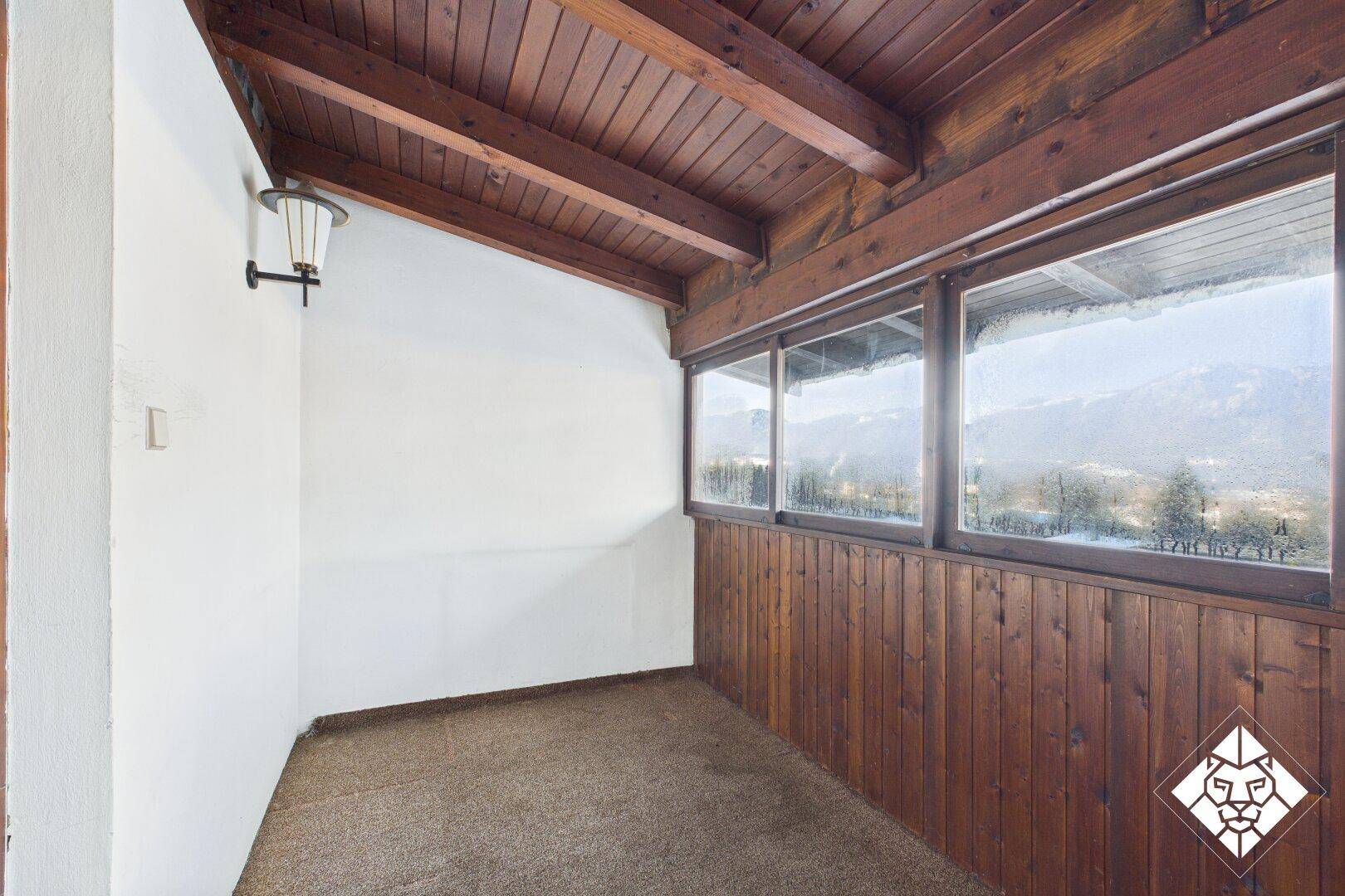 Überdachte Loggia mit Holzverkleidung und Fenstern, die einen weiten Blick bieten.