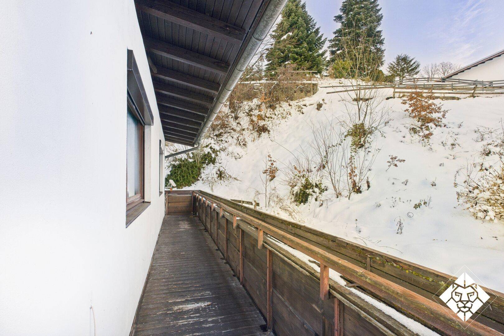 Schmaler Holzbalkon entlang der Hausseite mit Blick auf die schneebedeckte Landschaft.