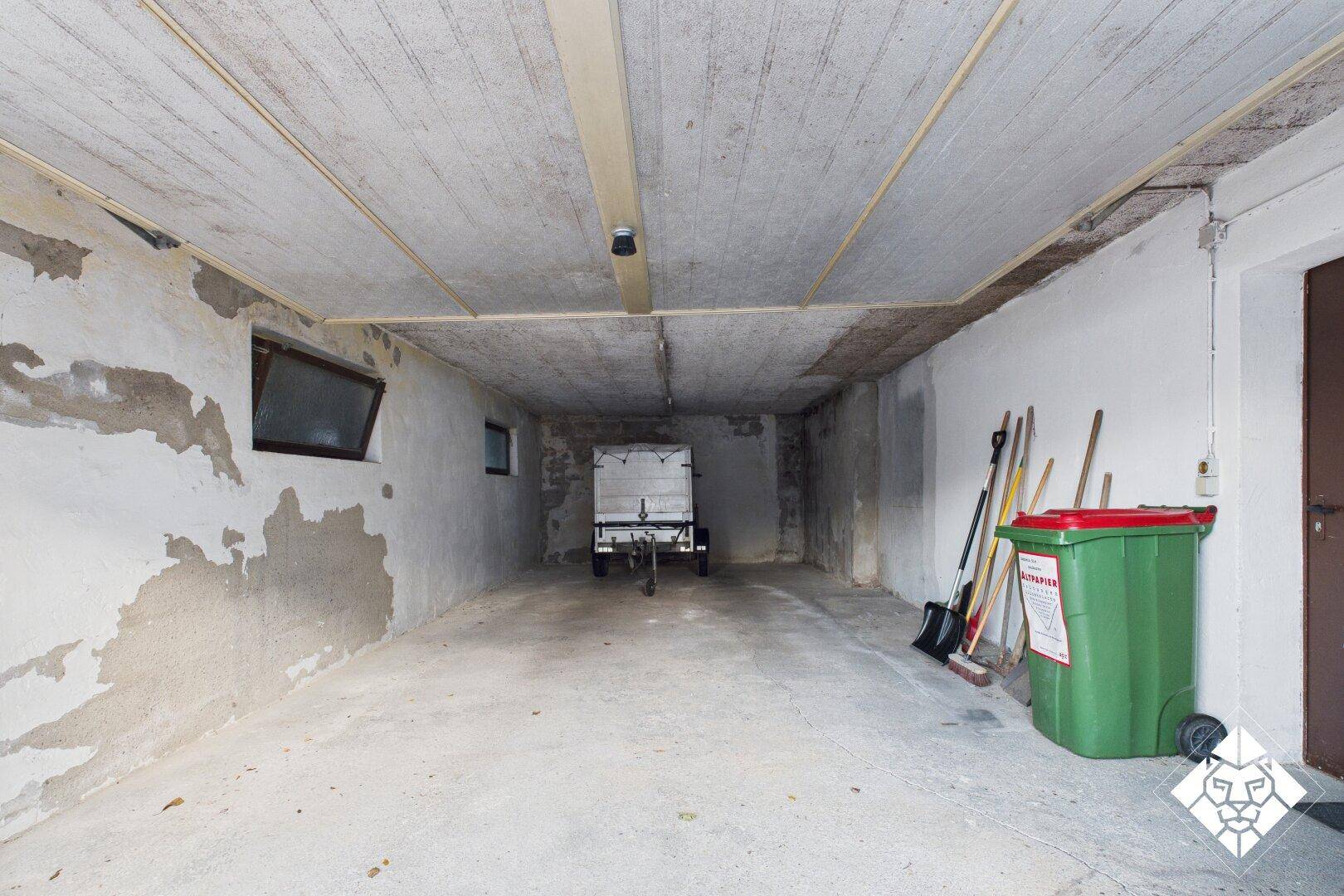 Geräumige Garage mit Betonboden und Stauraum für Fahrzeuge und Geräte.