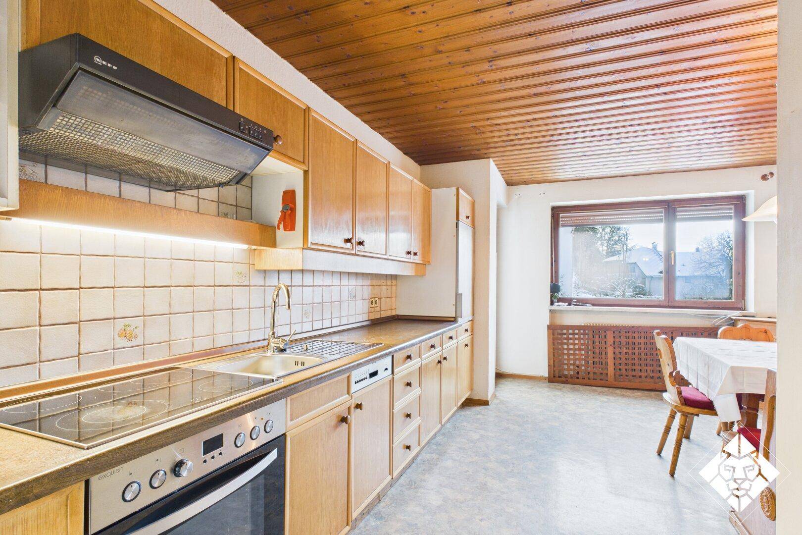 Traditionelle Küche mit Holzschränken, Fliesenboden und Essbereich am Fenster.