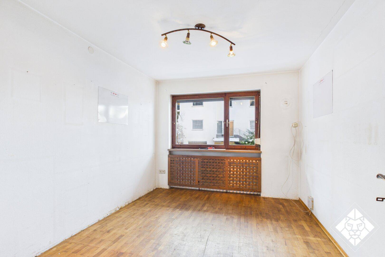Leeres Schlafzimmer mit Parkettboden und großem Fenster, das viel Tageslicht hereinlässt.