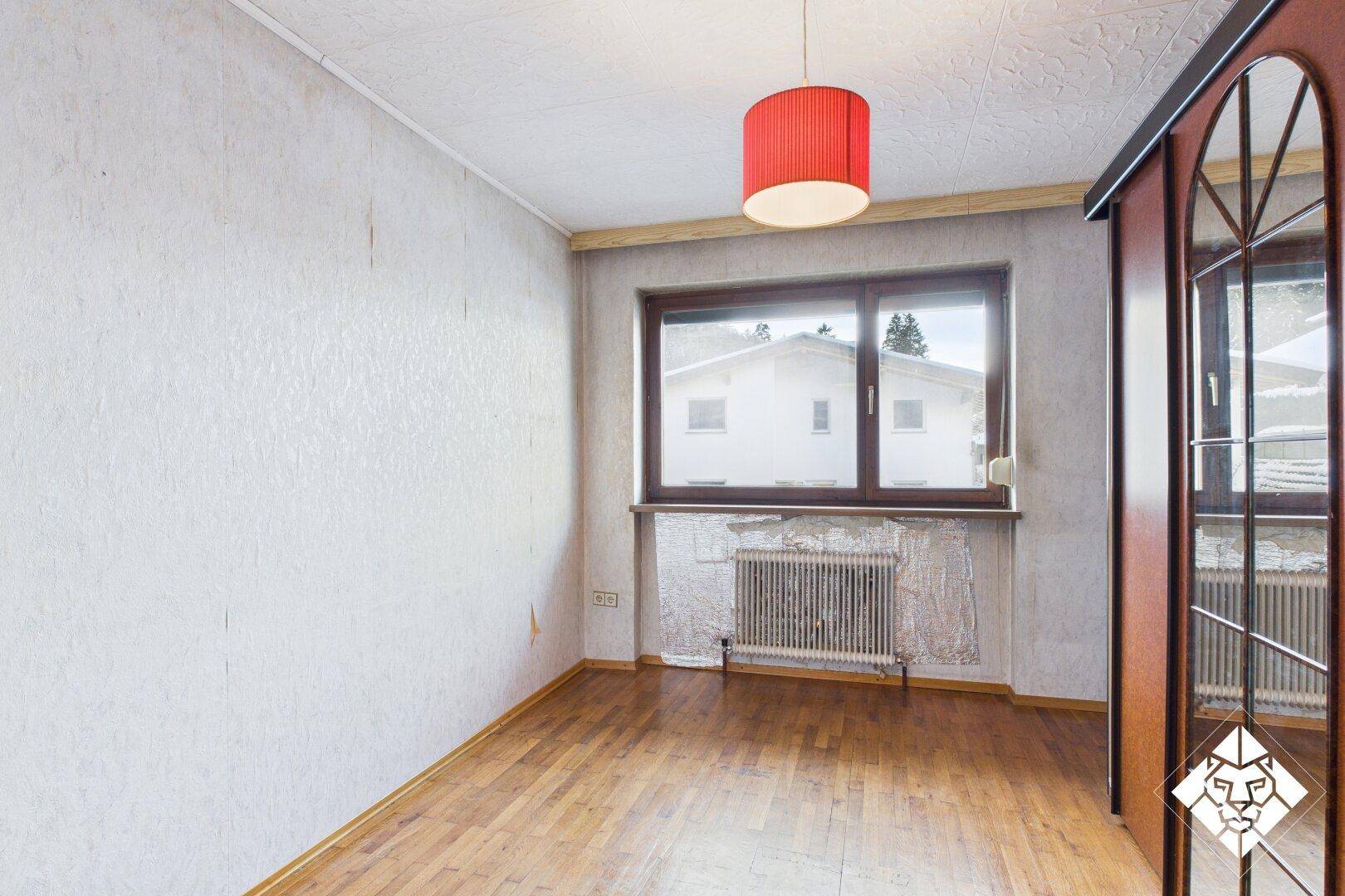 Schlafzimmer mit Parkettboden und Fenster, das den Blick nach draußen freigibt.
