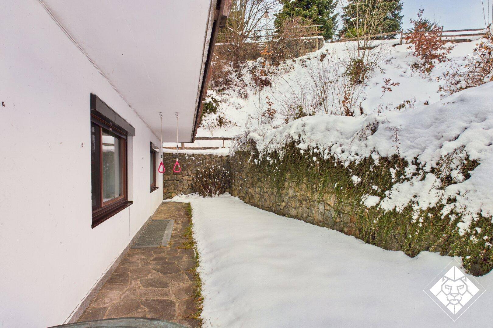 Seitlicher Gartenbereich mit Steinmauer und schneebedecktem Hang, bietet Privatsphäre.