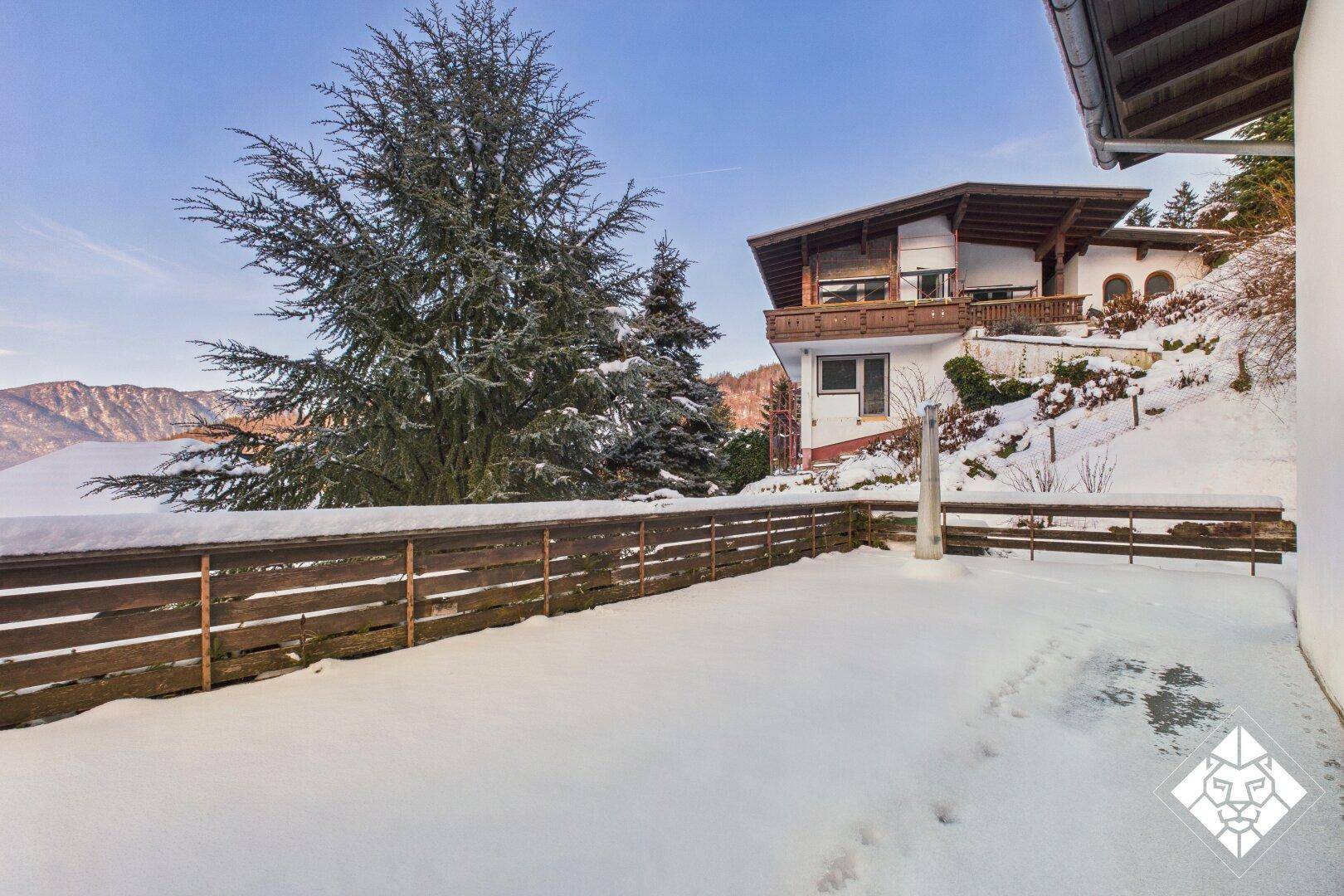 Große, schneebedeckte Terrasse mit Holzzaun und weitem Blick auf die Berge.