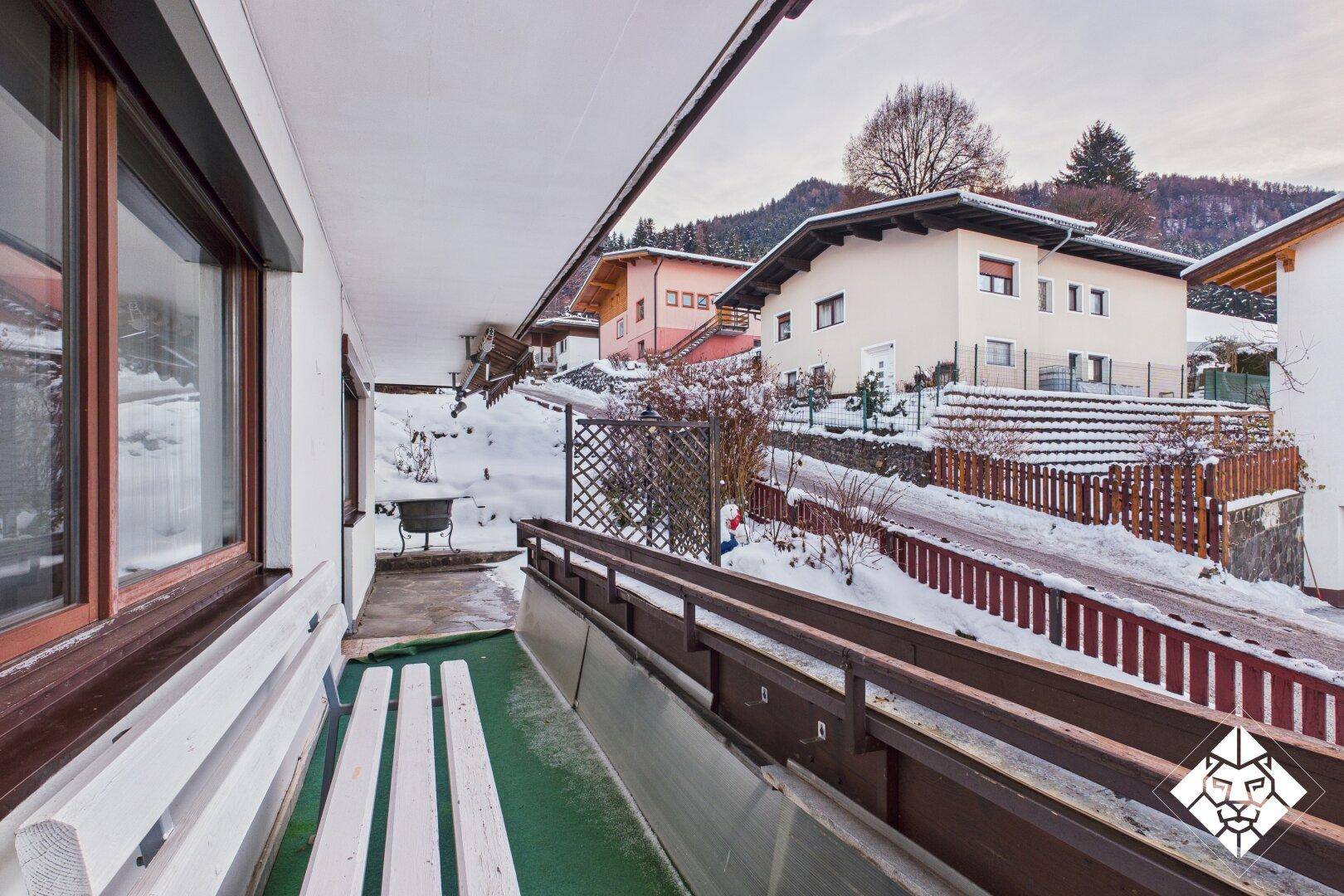 Überdachte Terrasse mit Sitzbank und Blick auf die verschneite Umgebung.