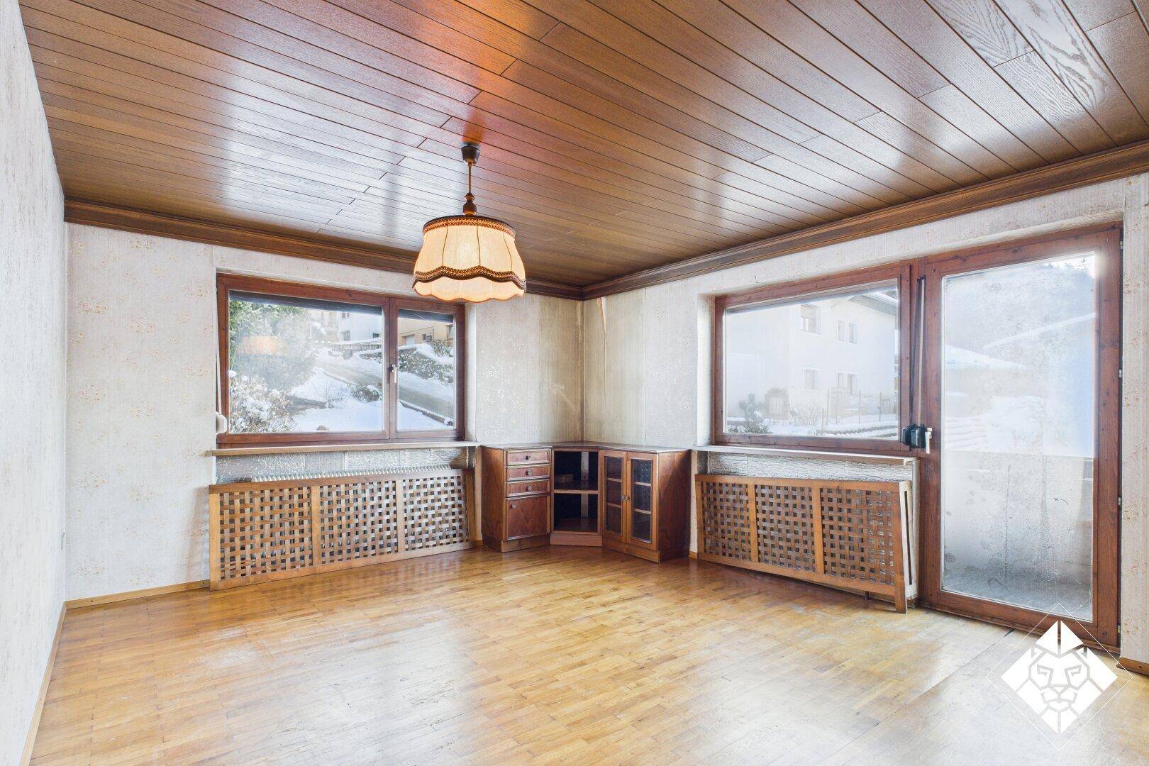 Geräumiges Wohnzimmer mit Parkettboden, Holzdecke und Zugang zu einem Balkon.