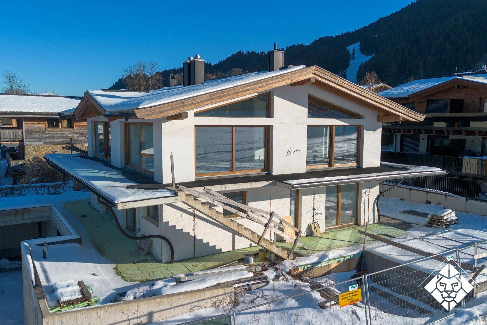 Neubau-Einfamilienhaus im Rohbau mit großen Fenstern und Blick auf die Skipiste.