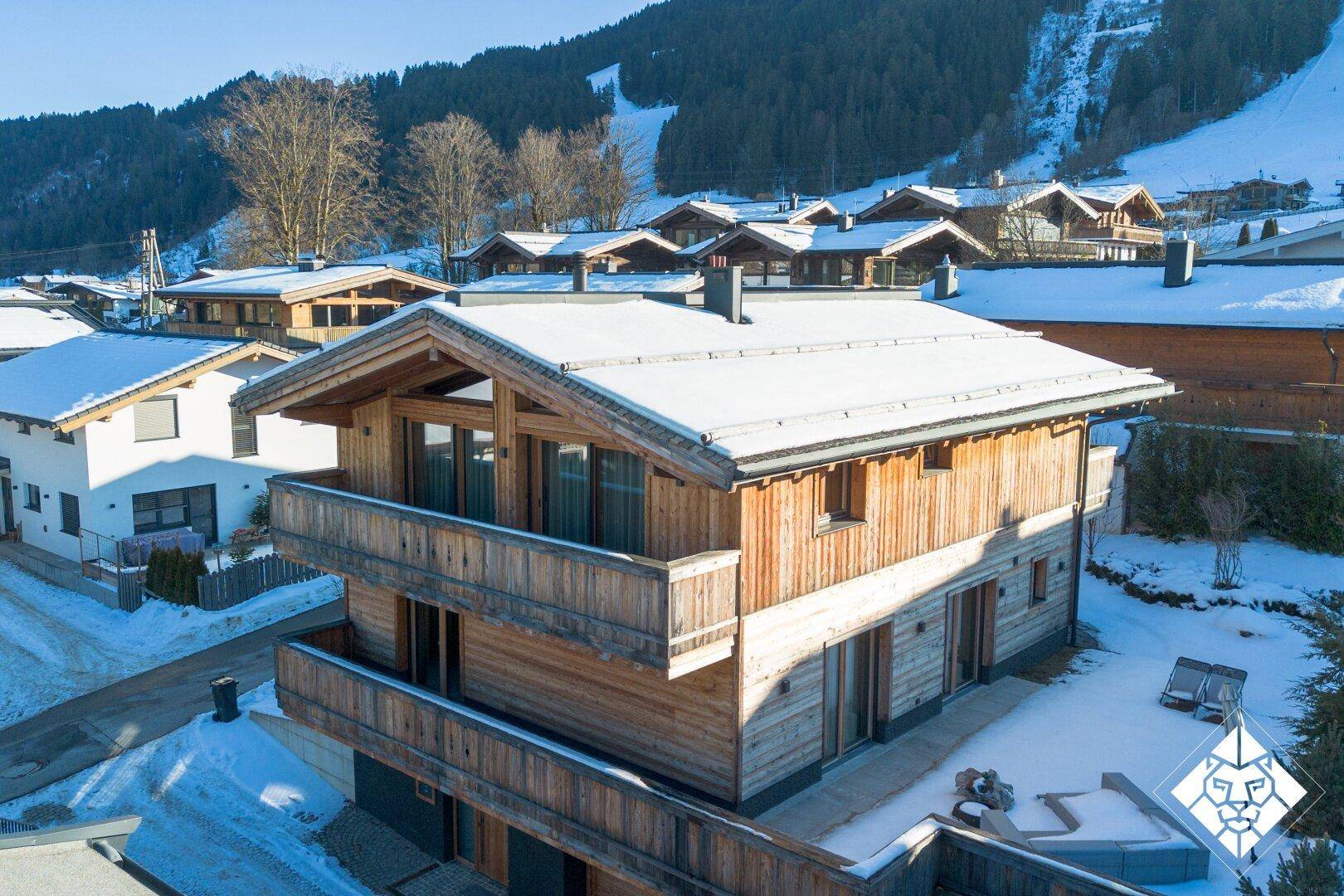 Charmantes Holzchalet mit schneebedecktem Dach und Balkonen vor einer malerischen Bergkulisse.