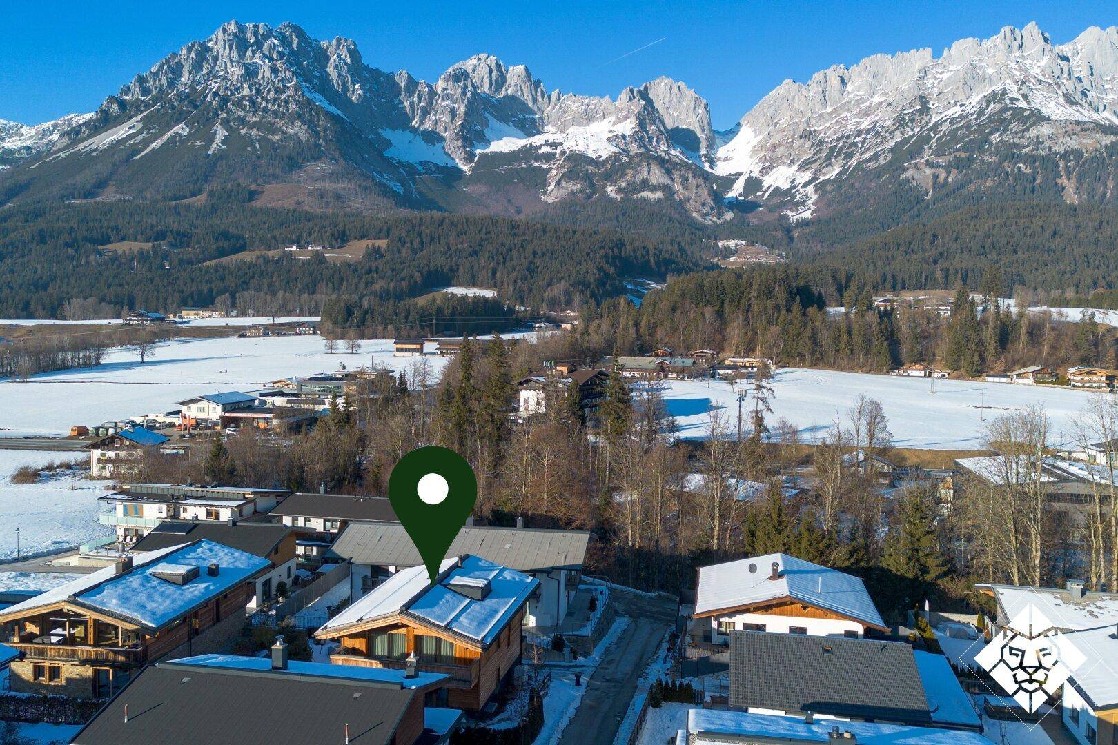 Weitläufige Luftaufnahme des Anwesens in einem verschneiten Bergdorf mit imposanter Bergkette im Hintergrund.