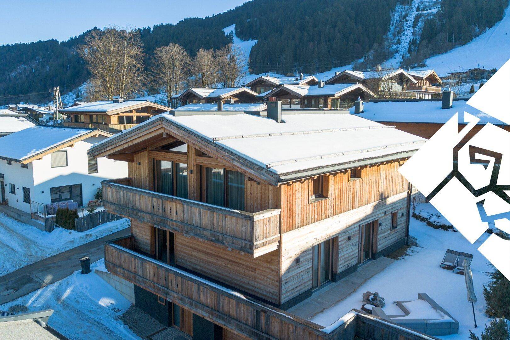 Charmantes Holzchalet mit schneebedecktem Dach und Balkonen vor einer malerischen Bergkulisse.