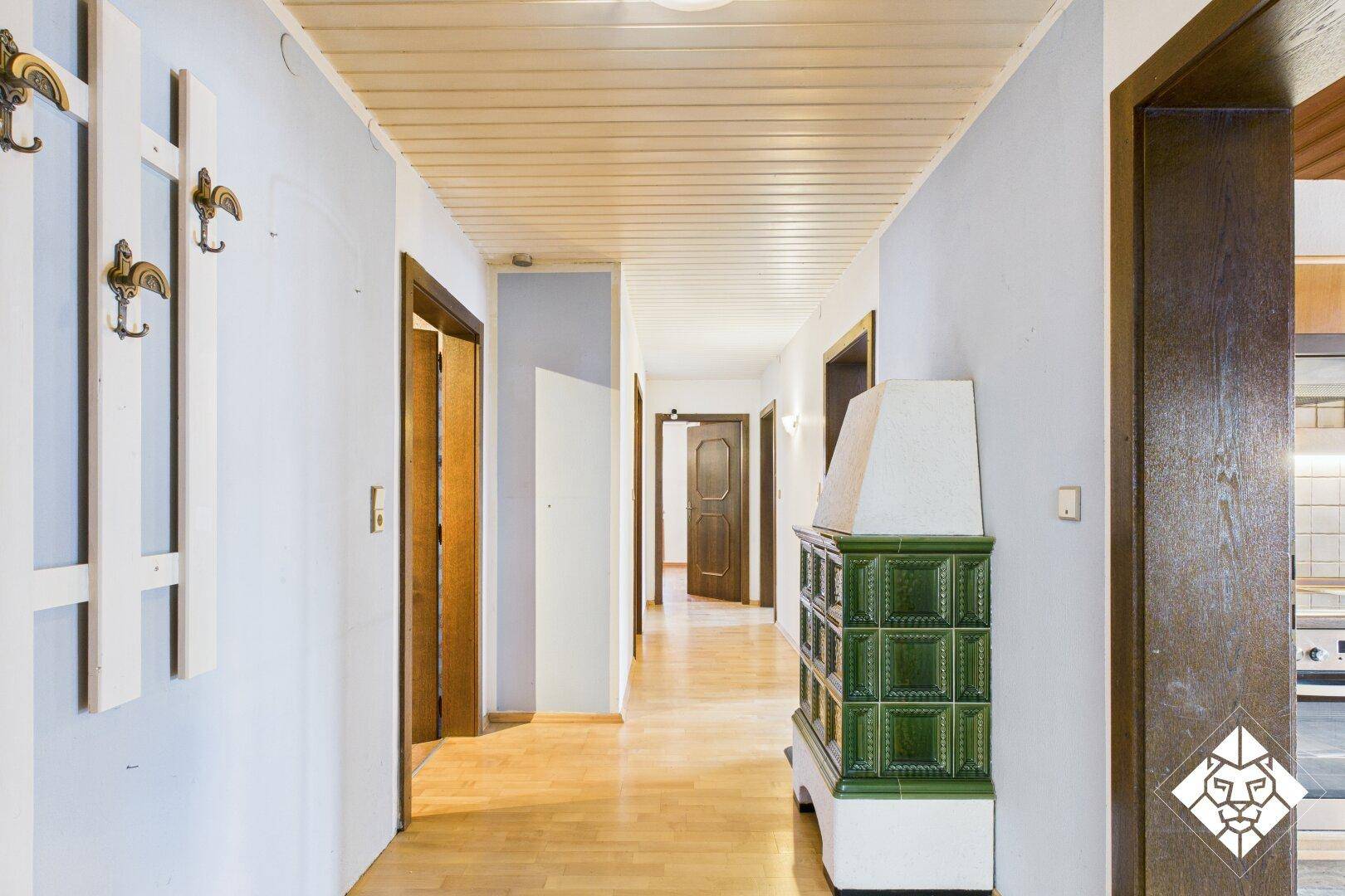 Heller Flur mit traditionellem Kachelofen, Holzdecke und Parkettboden, der zu mehreren Zimmern führt.