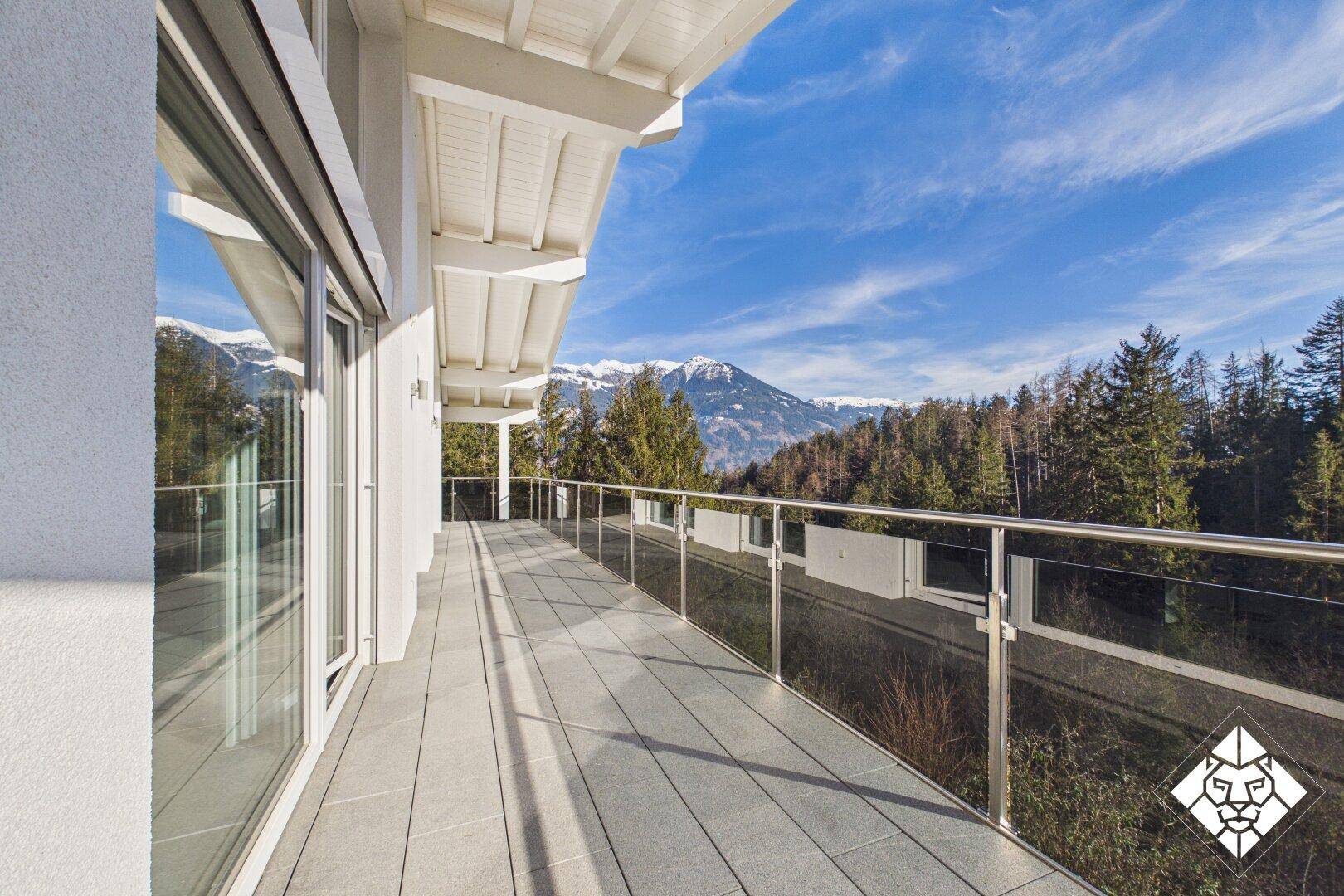 Geräumiger Balkon mit Glasgeländer und atemberaubendem Panoramablick auf die Berge und Wälder.