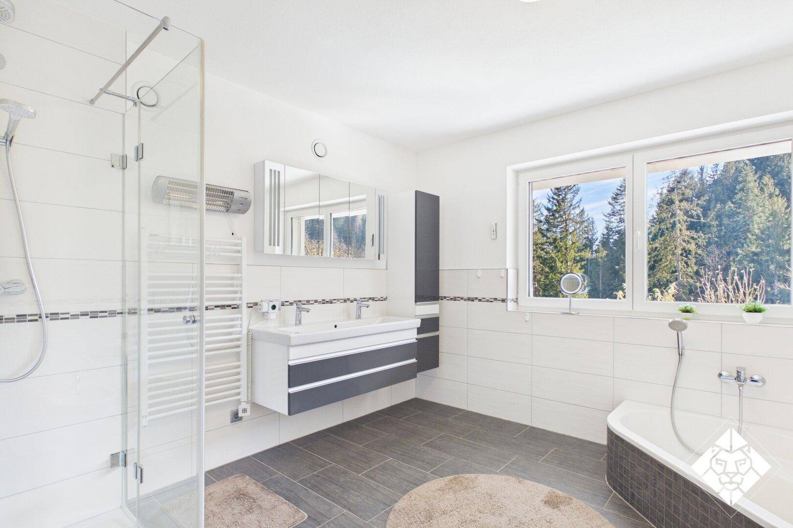 Modernes Badezimmer mit Doppelwaschbecken, Dusche, Badewanne und Fenster mit Waldblick.