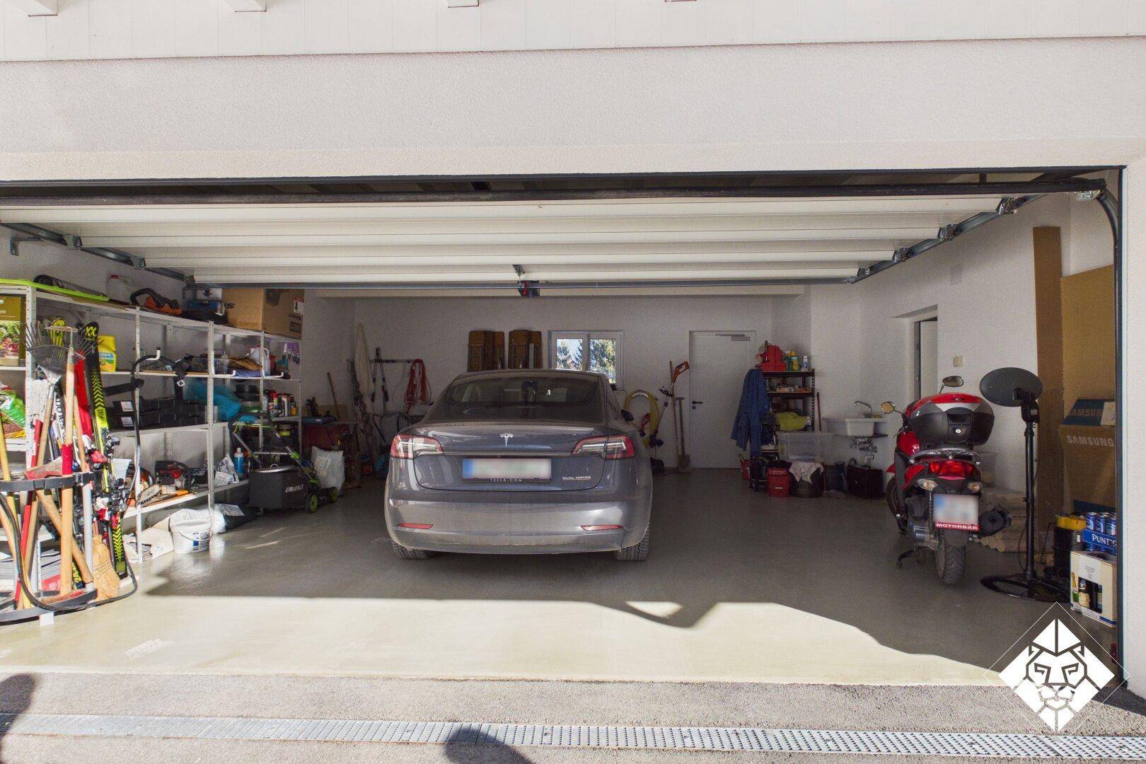 Geräumige Garage mit Platz für ein Auto und Motorrad, inklusive Abstellflächen und Regalen.