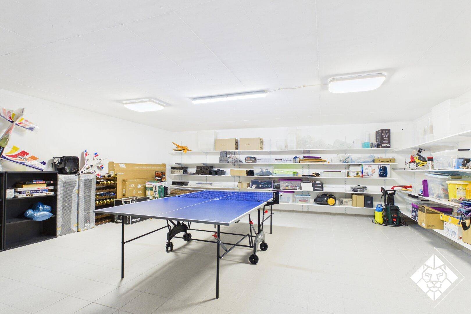 Großer Hobbyraum mit Tischtennisplatte und Regalen für vielseitige Nutzung und Lagerung.