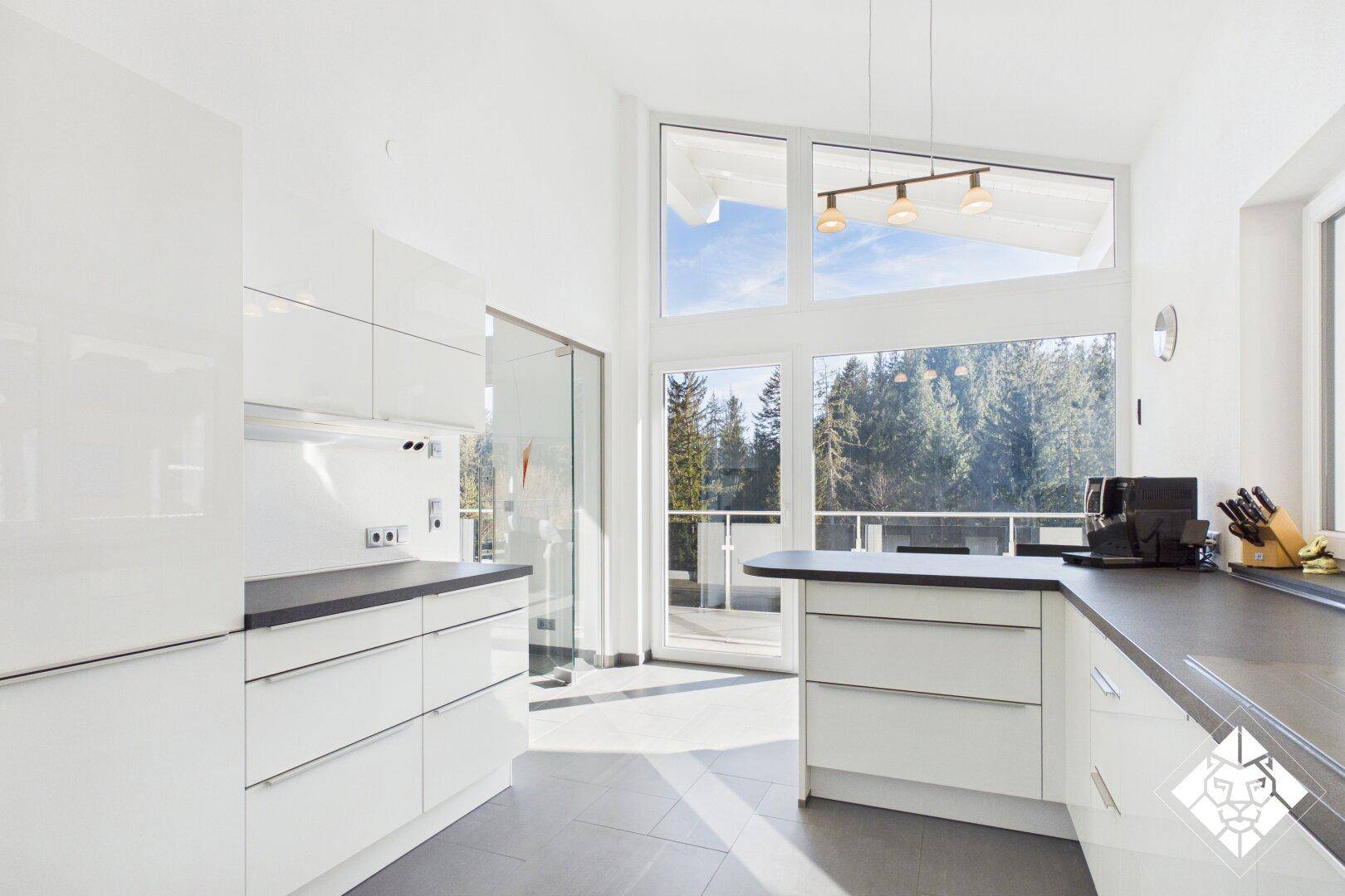 Moderne weiße Küche mit Hochglanzfronten, dunkler Arbeitsplatte und Zugang zum Balkon.