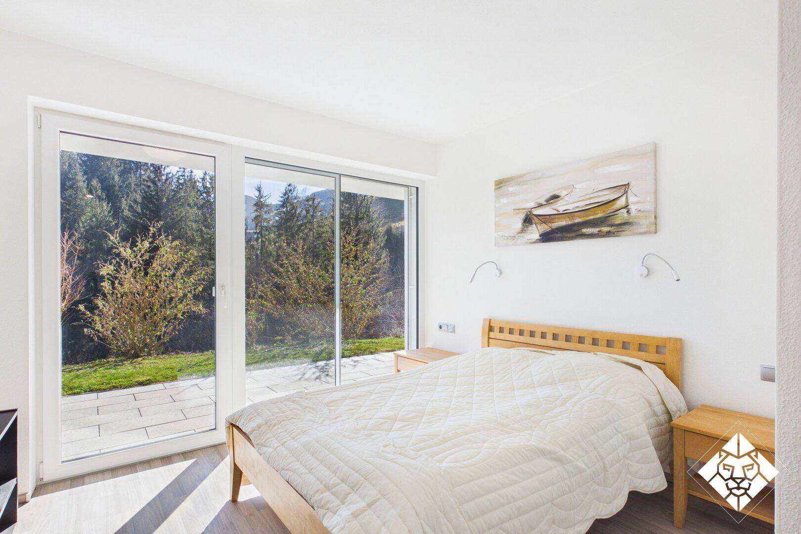 Helles Schlafzimmer mit Holzbett, Parkettboden und großen Fenstern mit Zugang zur Terrasse.