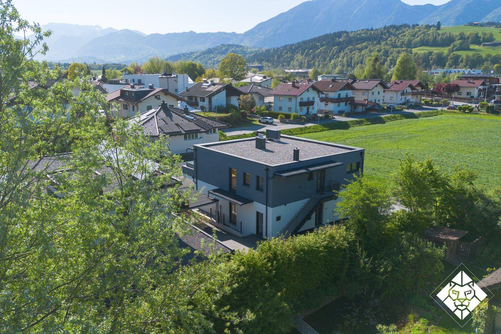 Das moderne Gebäude von oben, umgeben von weiten grünen Feldern und einer beeindruckenden Bergkulisse.