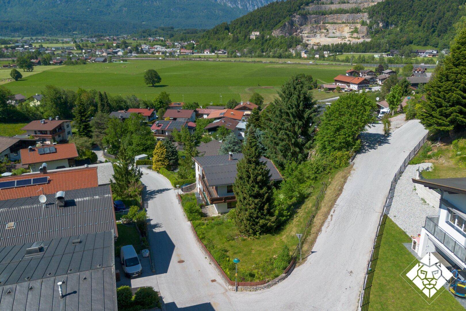 Luftaufnahme einer Wohnsiedlung in ländlicher Umgebung mit beeindruckendem Bergpanorama im Hintergrund.