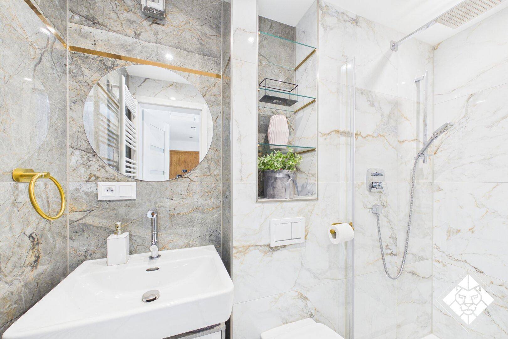 Modernes Badezimmer mit hellen Marmorfliesen, rundem Spiegel und Dusche.